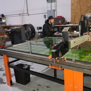 a man sitting at a laptop in front of a metal cutter